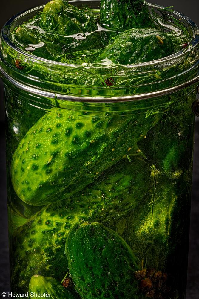 Банка с маринованными огурцами крупным планом; зелёные огурцы, укроп и специи в рассоле видны сквозь прозрачное стекло, яркие текстуры.