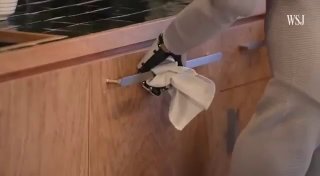 Робот NEO выполняет уборочную задачу на кухне: манипулятор держит тряпку и протирает поверхность, демонстрируется возможность работы с дверцами и шкафами.