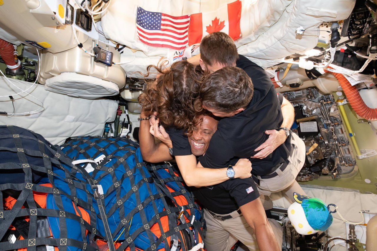 Экипаж миссии «Артемида‑2» обнимаются внутри капсулы «Орион», на заднем плане видны оборудование, стропы и частично американский флаг.