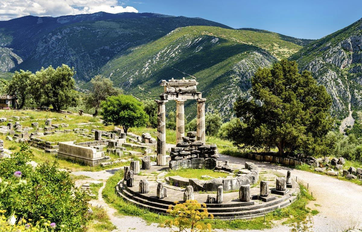 Руины древнего святилища на холме: круглая постройка и остатки колонн на фоне горного пейзажа и долины в глубине.