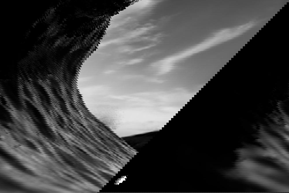 Монохромная фотография большой морской волны в динамике: игра света и тени по изгибу воды, драматичный низкий ракурс