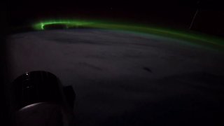 Зелёное «танцующее» полярное сияние над ночной стороной Земли, снятое с борта корабля Crew Dragon; видна часть корпуса и облачная поверхность.