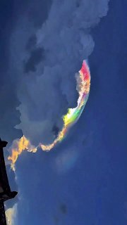 Яркая иризация на краю облака в тёмном небе: радужная полоска с красными и зелёными тонами на облачной структуре.