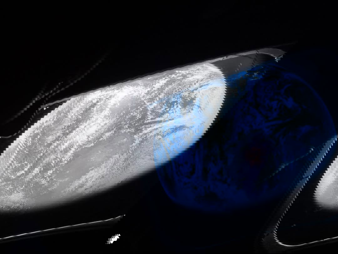 Тёмный профиль астронавта на фоне иллюминатора «Орион», в окне — вид земного диска с облачными системами на фоне космической тьмы.