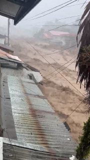 Наводнение и поток грязи в поселке на Филиппинах после проливного дождя: размытая дорога, мусор и затопленные крыши на переднем плане.