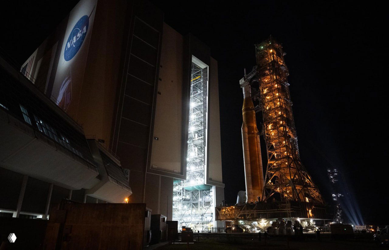 Ракета SLS у стартовой башни ночью, освещение технического оборудования и доступные рабочие площадки — ночной вид подготовительного этапа.