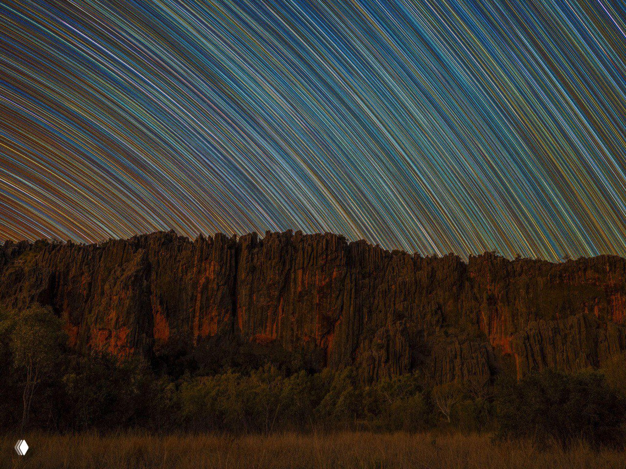 Панорамный пейзаж с горной линией на переднем плане и сотнями следов звёзд по небу, длительная выдержка создаёт полосы от движения небесных тел