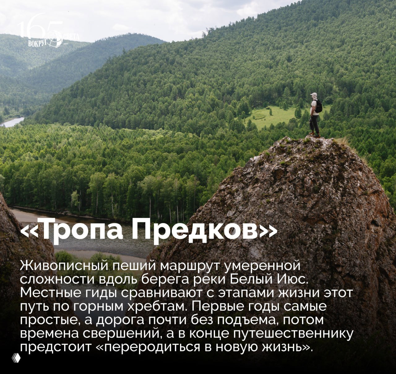 Турист стоит на скале над лесистой долиной и рекой на маршруте «Тропа Предков»: вид на горные хребты, зелёные леса и извилистую реку.