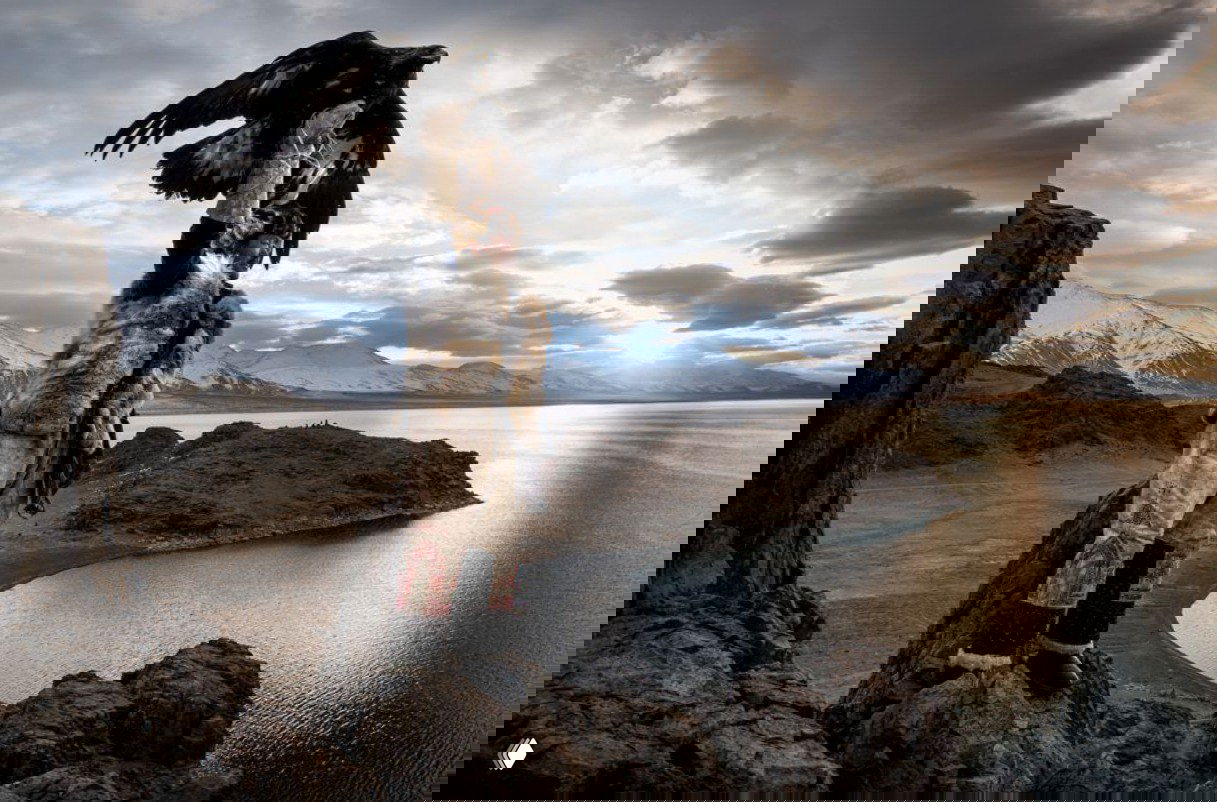 Кадр охотника с беркутом на руке на утёсе у горного озера: величественный пейзаж, суровые горы и отражение воды подчёркивают масштаб сцены.