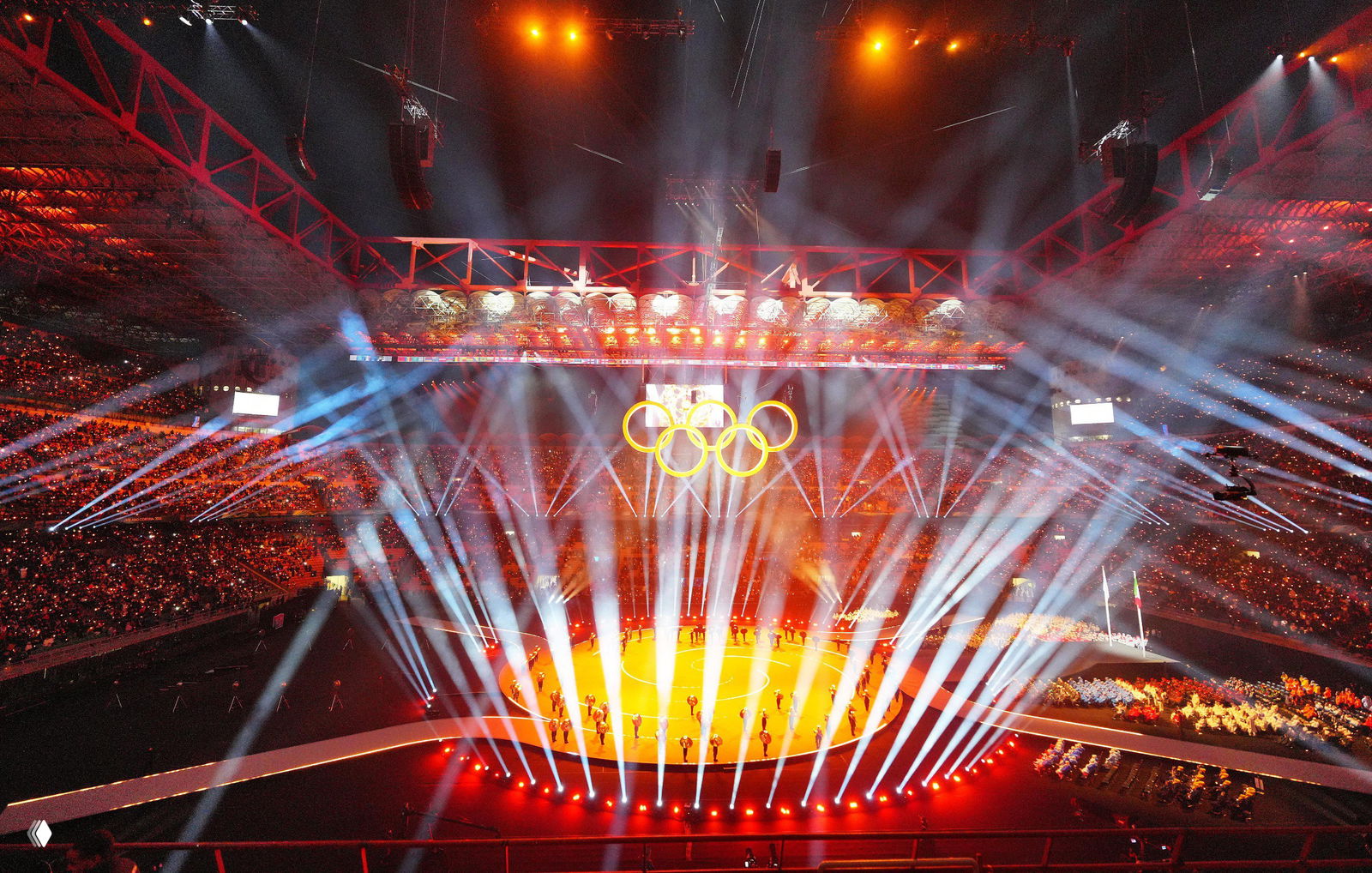 Общий план стадиона «Сан‑Сиро» с освещённой ареной, зрители на трибунах и пятью олимпийскими кольцами — финальная часть церемонии открытия.
