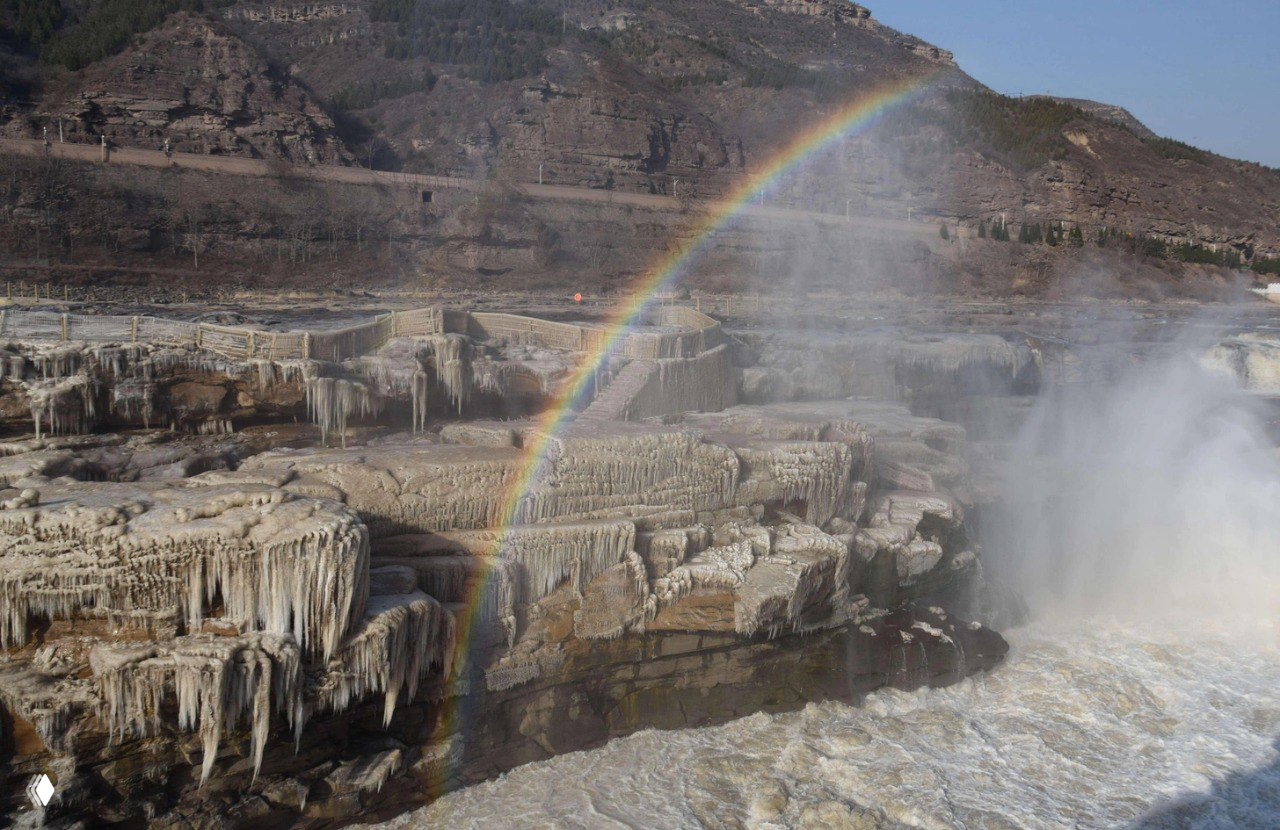 Радуга над частично замёрзшим 20-метровым водопадом Хукоу на реке Хуанхэ: ледяные террасы, туман и цветная арка в морозный день.
