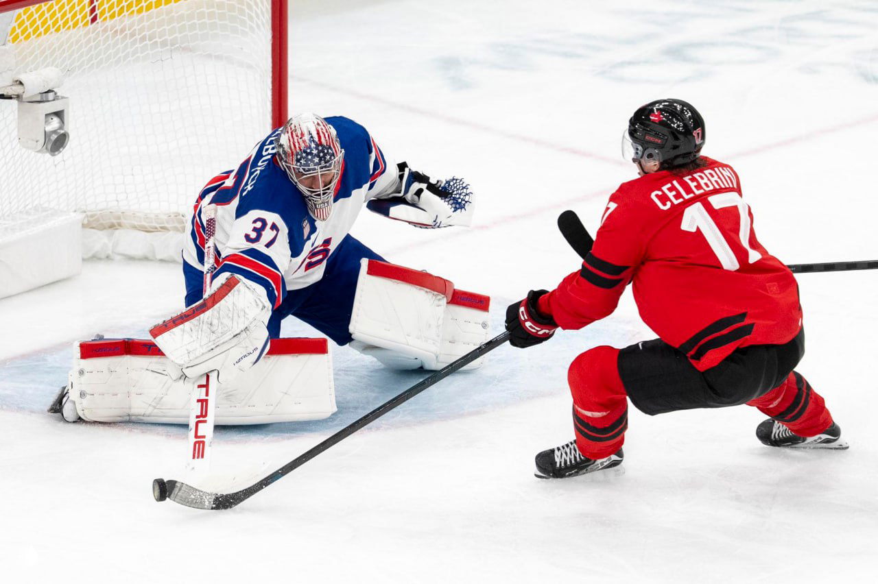 Вратарь сборной США в защитной экипировке отражает бросок игрока сборной Канады на льду во время решающего финального матча Олимпиады в Милане.