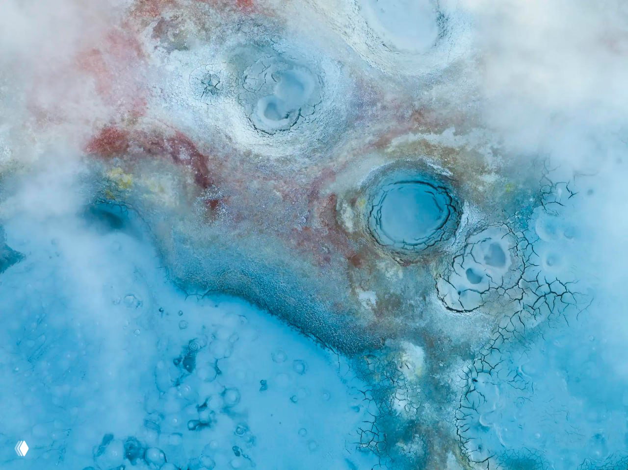 Воздушный снимок геотермальных и водянистых образований: бирюзовые круги, текстуры и трещины на светлой поверхности, снято с высоты.