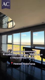 Вертикальный кадр панорамного окна квартиры с видом на город и Волгу, рассветное небо видно через стекло, на фото логотип агента.