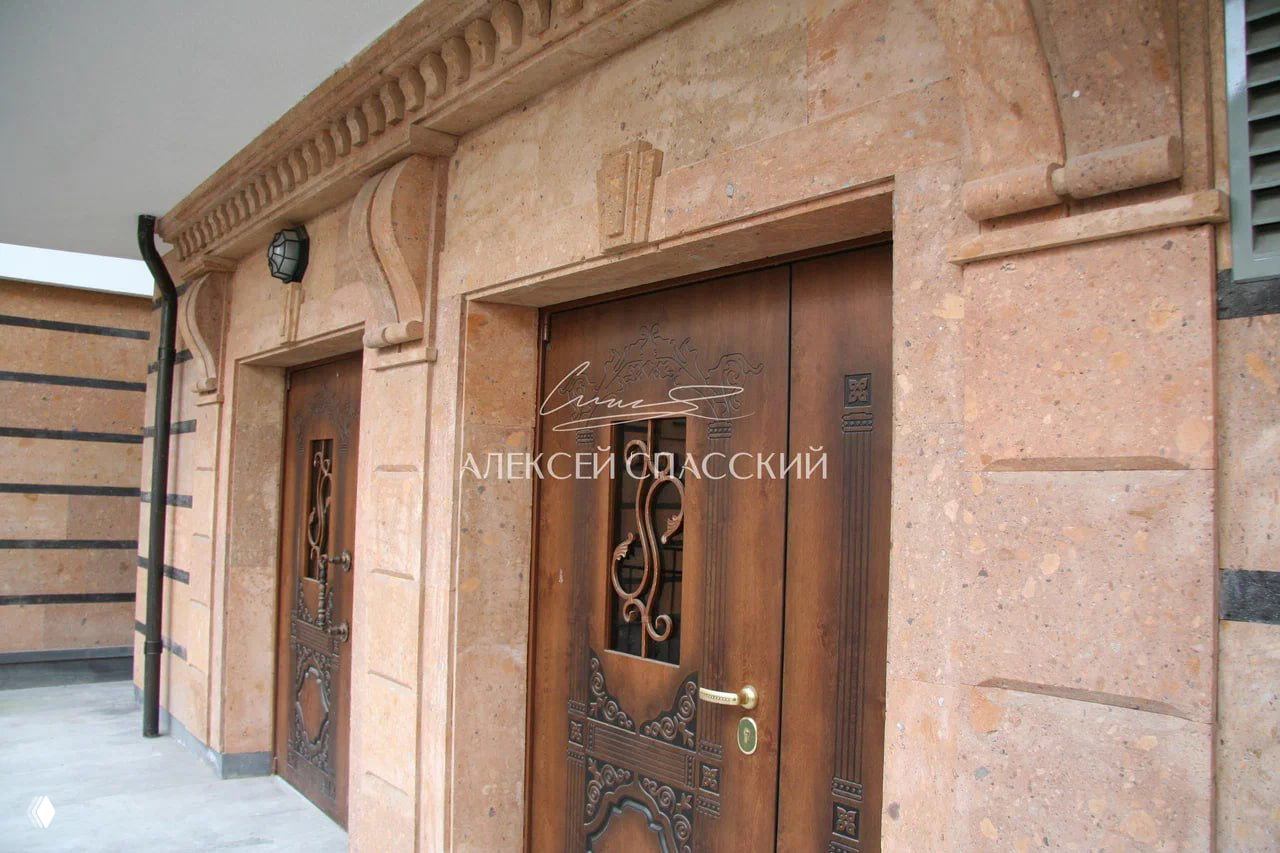 Детали парадного входа: декоративная каменная отделка, деревянные двери с резьбой и элементы архитектурного декора у входа в здание.