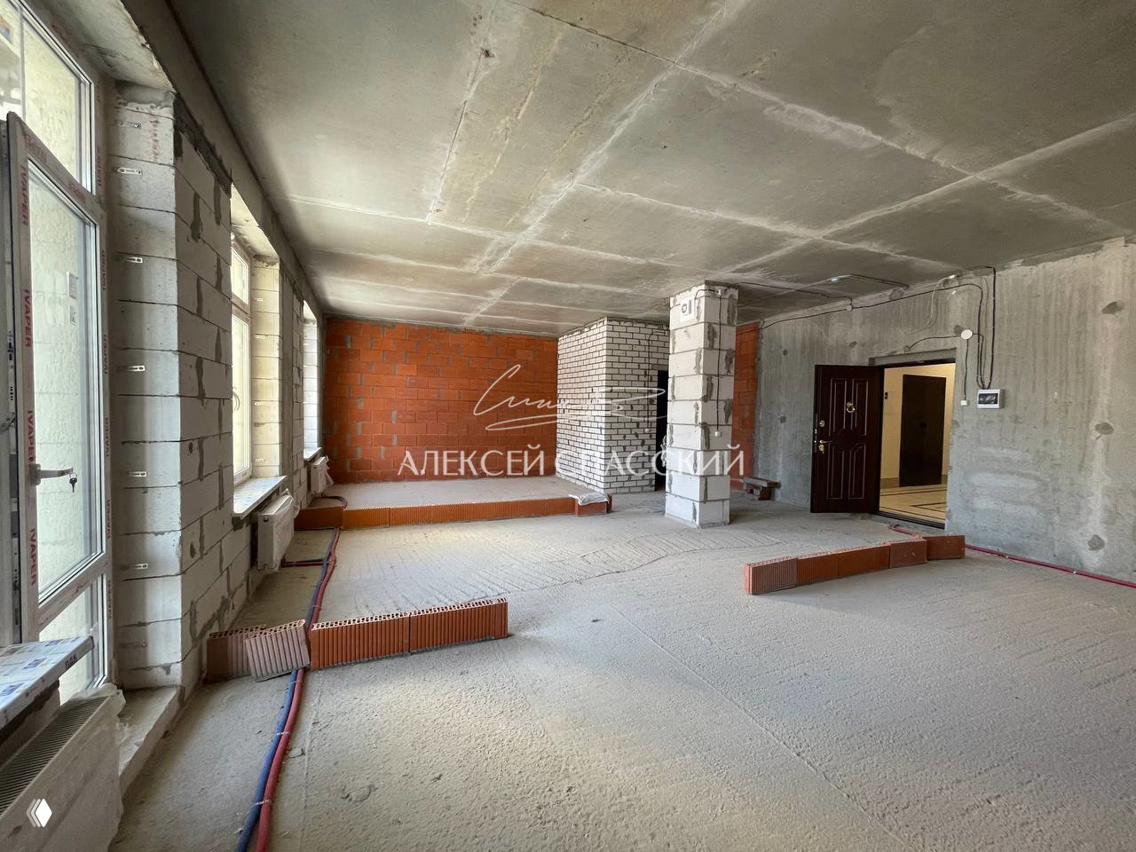 Пустая квартира без чистовой отделки: просторное помещение с панорамными окнами, черновая стяжка пола и ограждения для будущих перегородок.