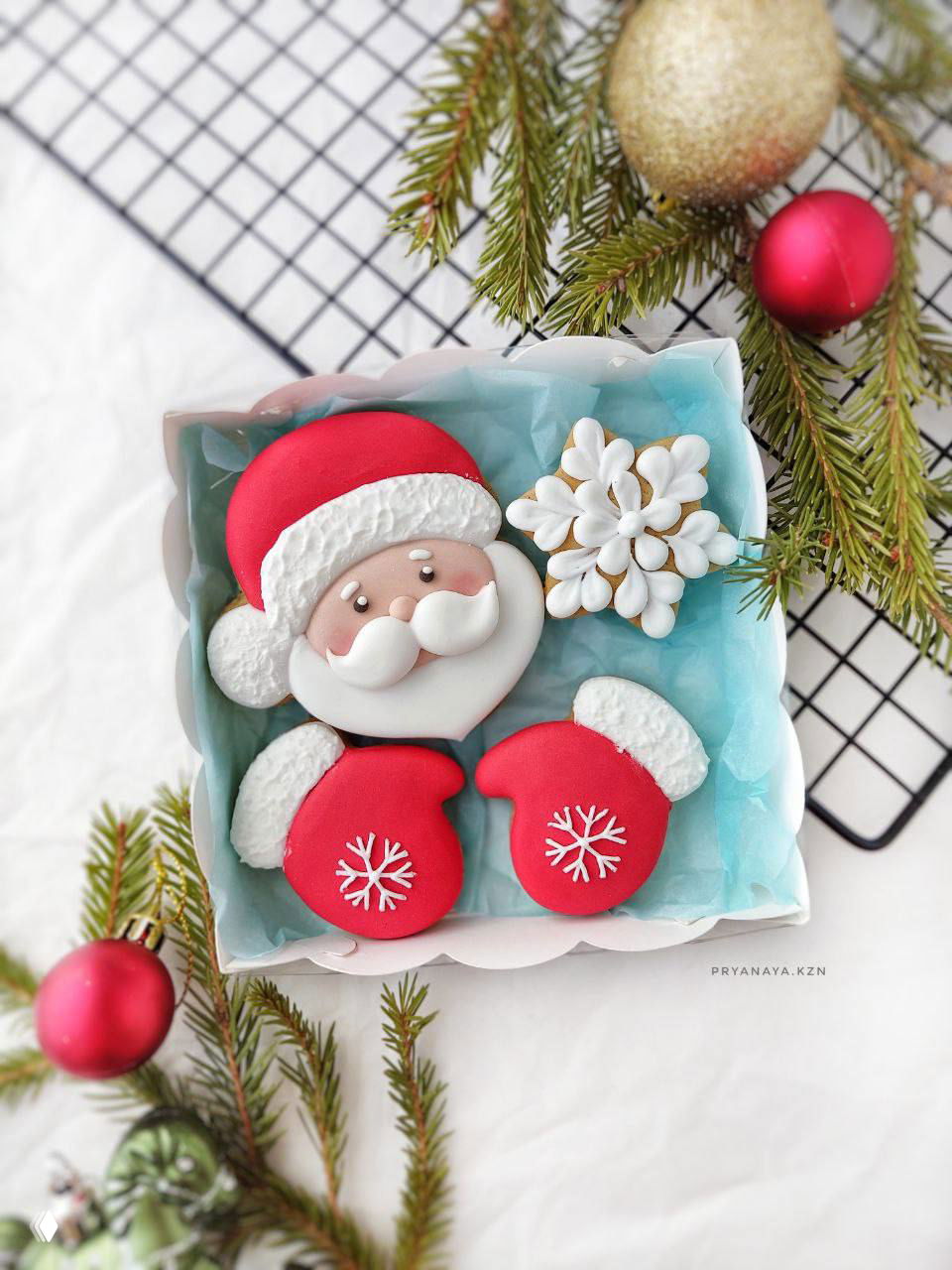 Коробочка с пряником в виде Деда Мороза, снежинкой и красными варежками, оформленная еловыми ветками и праздничными украшениями.