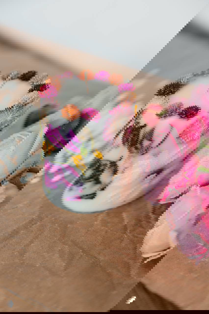 Низкая белая свеча с декоративными засушенными цветами вокруг и рядом розовые бутоны на крафтовой бумаге — праздничная композиция мастера.