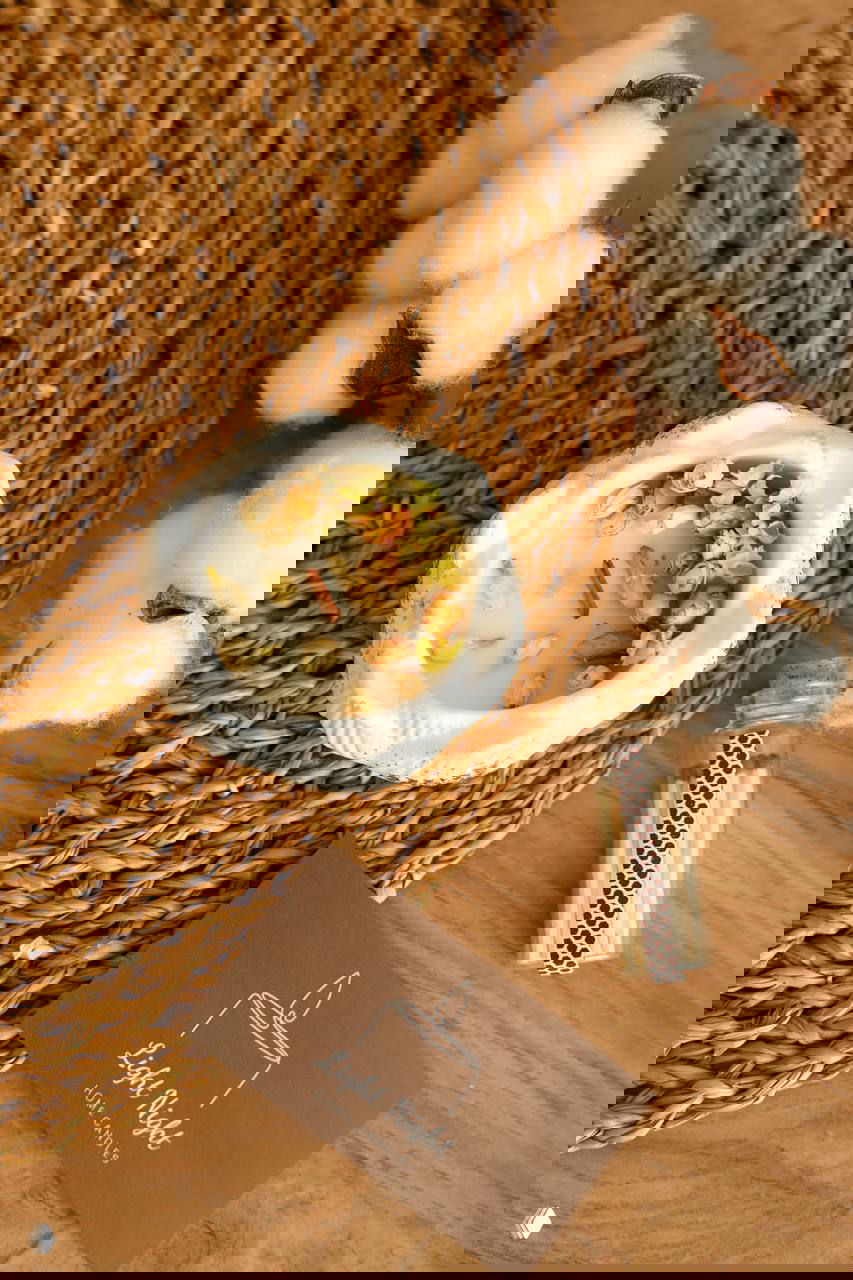 Небольшая свеча в керамической миске с добавлением трав и засушенных бутонов, рядом коробочка со спичками и декоративные хлопковые ветки.