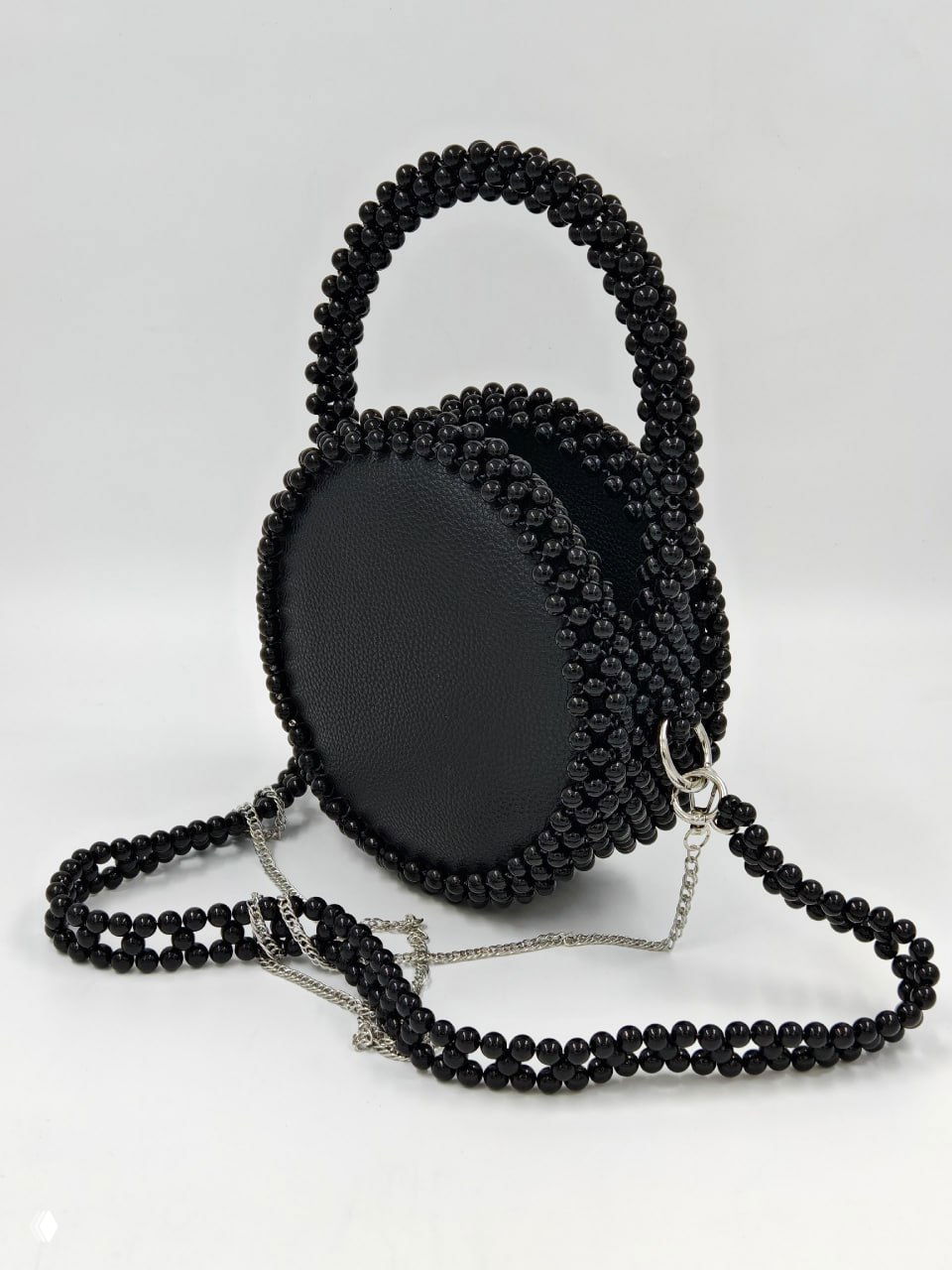 Черная сумка из бусин в круглой форме с длинным ремнём из тех же бусин, сфотографирована на белом фоне для каталога.