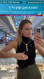 Зеркальное селфи в бутике Rosone: женщина примеряет крупное золотое колье и серьги Claudio Canzian на фоне подсвеченных витрин и прилавков.