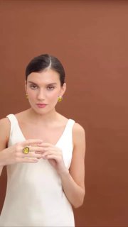 Портрет модели в светлом топе, демонстрирующий комплект FIORE DI FIRENZE: янтарное кольцо и серьги на нейтральном коричневом фоне.