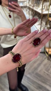 Руки с крупными кольцами с насыщенными красными камнями демонстрируют вариант Filigrana на фоне витрины и полок с украшениями в магазине.
