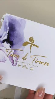 Крупный план: рука держит коробку Fiore di Firenze с фиолетовым акварельным принтом и золотым логотипом — распаковка украшений.