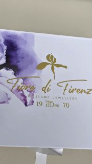 Лицевая часть коробки Fiore di Firenze крупным планом: логотип и фиолетовый акварельный элемент на белом фоне.