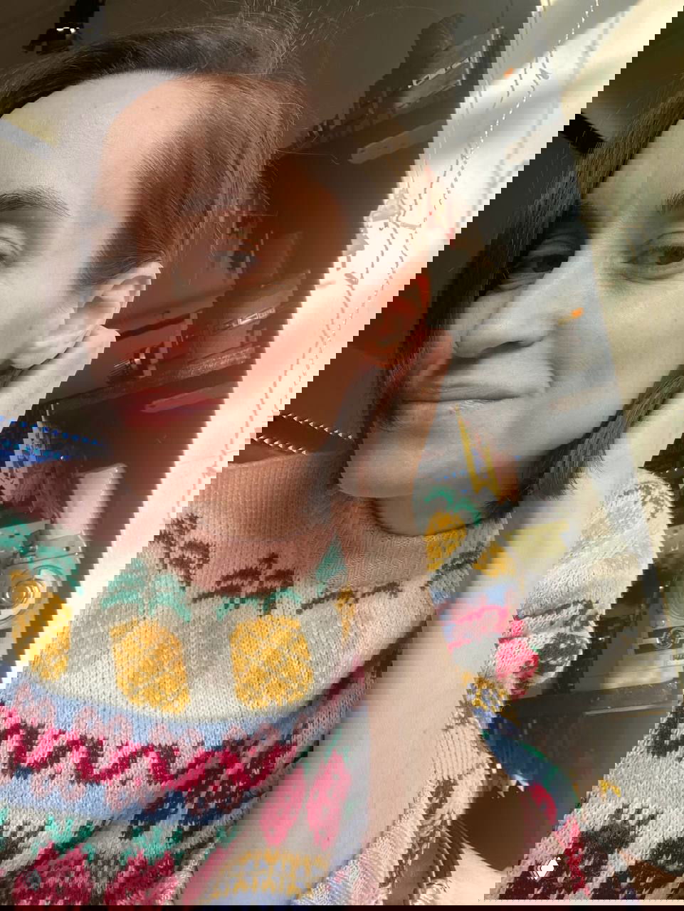 Портрет женщины в том же свитере, рука у лица, тёплый солнечный свет и видимые элементы студийного оборудования на заднем плане.