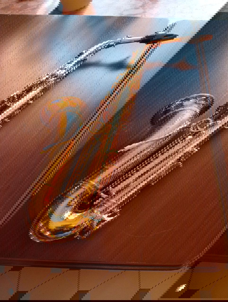 Золотистый саксофон, положенный на деревянный стол в кафе — реквизит для музыкального номера или элемент атмосферы вечера выступлений.