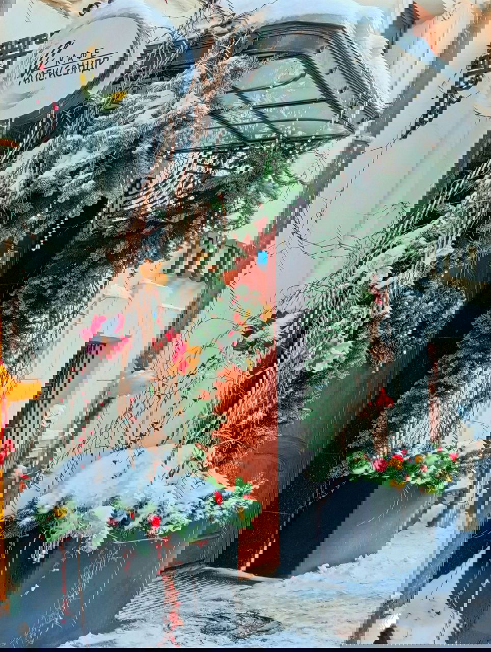 Декорированный зимний вход в кафе «Александр» с еловыми гирляндами и снежными украшениями у входной двери ресторана.