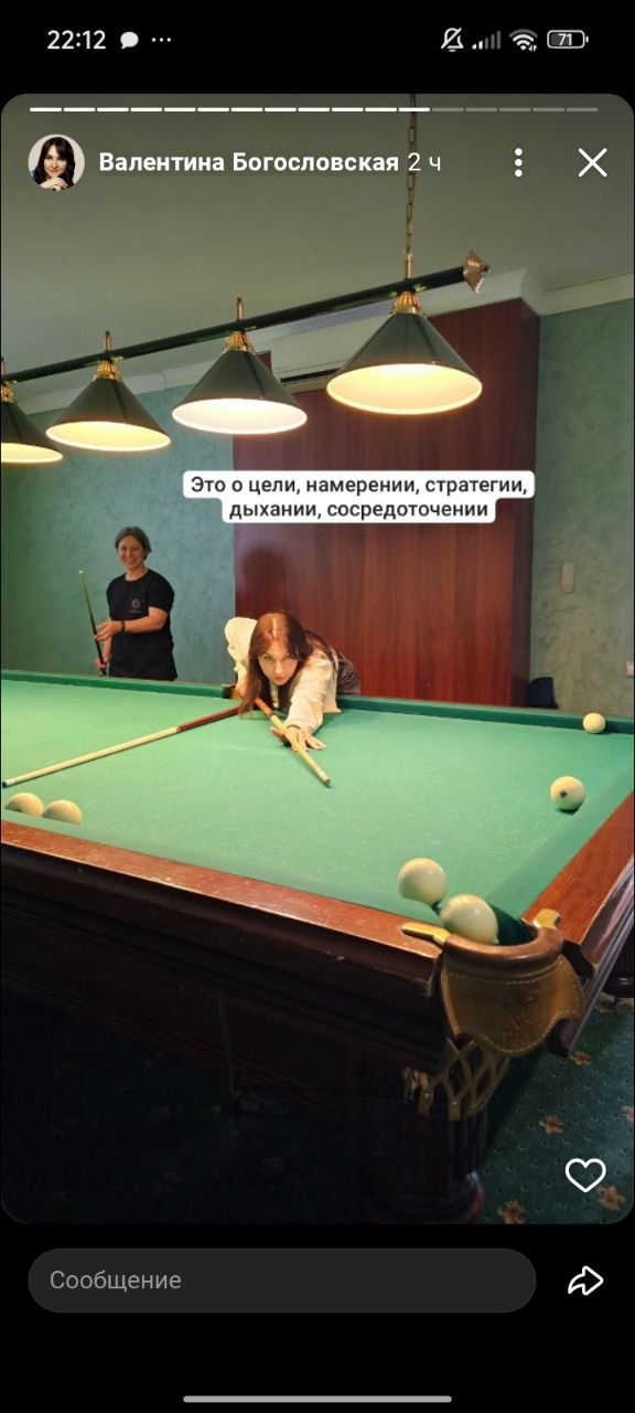 Женщина делает удар кием по шару на бильярдном столе; в кадре видны другие участницы и интерьер зала с характерными лампами над столом.