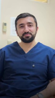 Портрет врача Алиева Равана Гахрамановича в кабинете клиники ЕМЦ: в синей медицинской форме, спокойная улыбка, фон — интерьер медицинского кабинета.