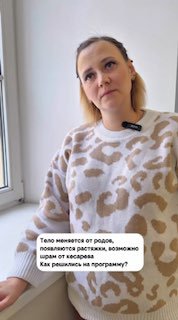 Суррогатная мама Зина у окна в свитере с микрофоном, отвечает на вопросы о программе суррогатного материнства.