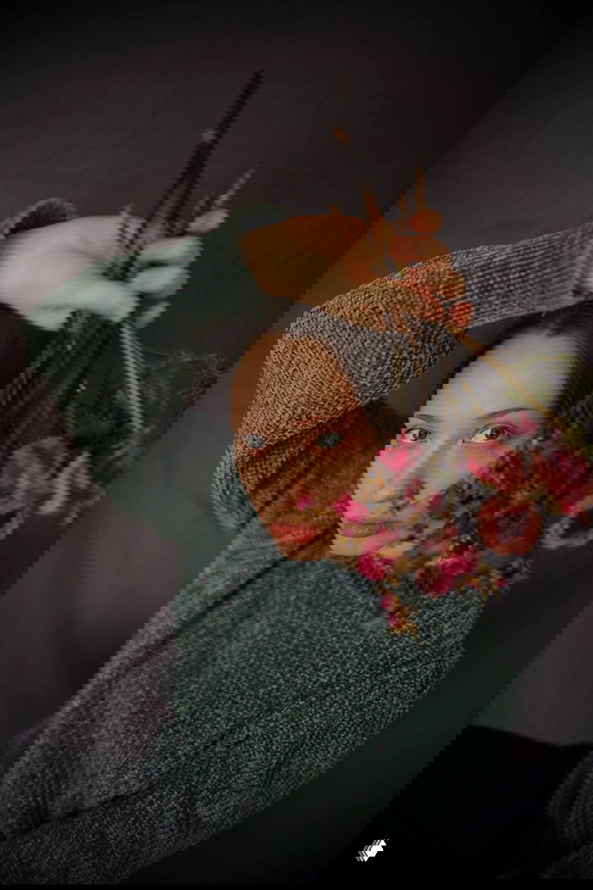 Портрет женщины в сером свитере, держащей засохшие цветы перед лицом; изображение передаёт личную магнетичность и внутреннюю выносливость