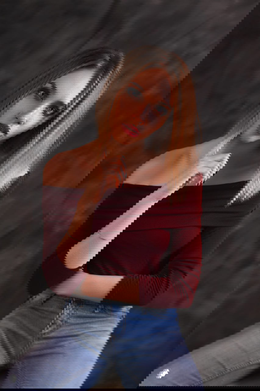 Студийный портрет молодой женщины в бордовом топе и джинсах, нейтральный фон; иллюстрация к посту об астрологической услуге