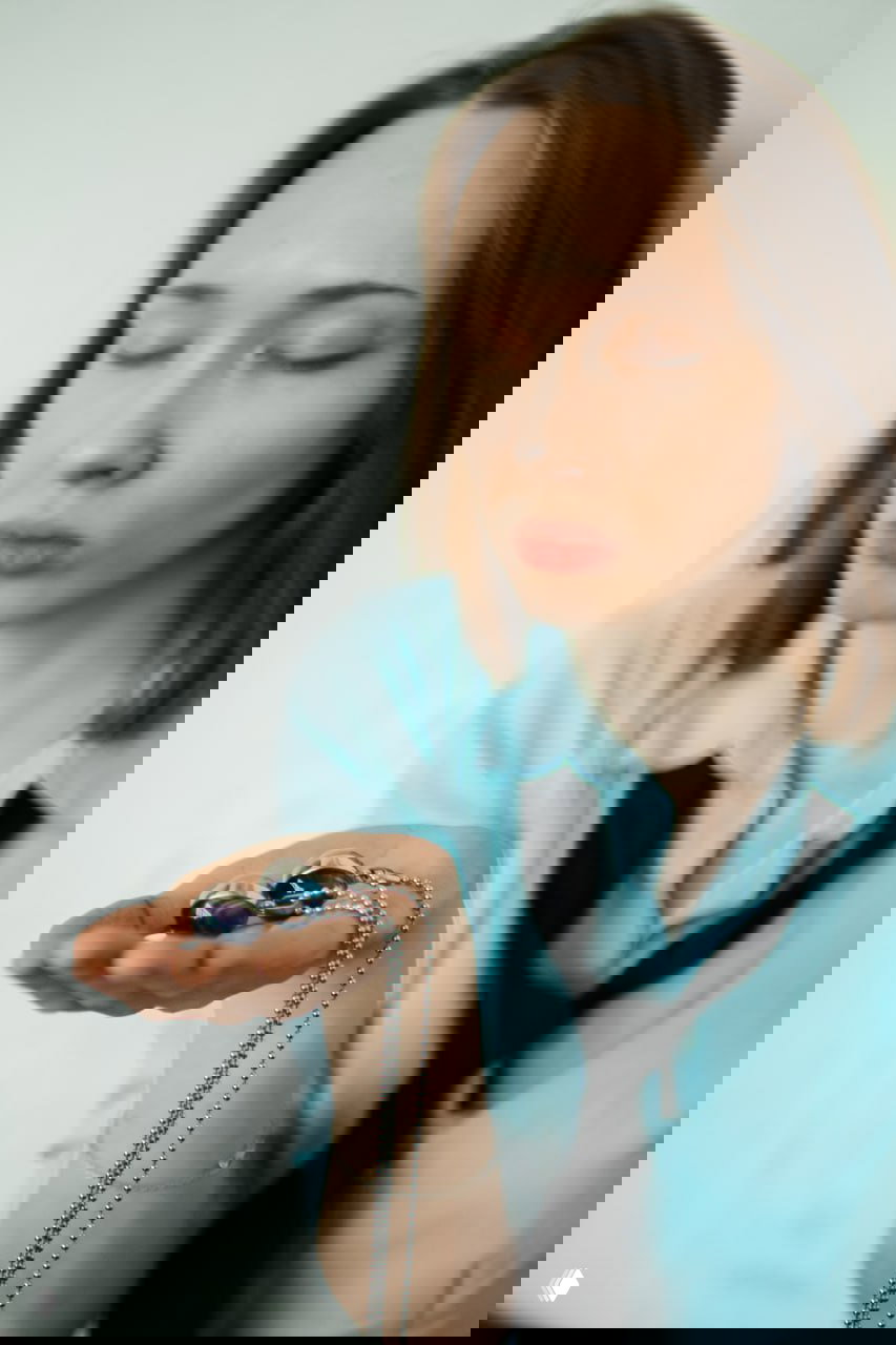 Портрет женщины с закрытыми глазами, держащей в ладони подвески на цепочке; фото создает атмосферу личной и интимной консультации астролога.