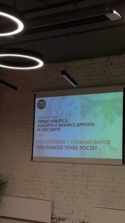 Фото зала: проекционный экран с презентацией, подвесные кольцевые светильники и кирпичная стена — кадр с гостевого дня ТОП‑клуба и открытого Совета директоров.