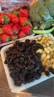 Поднос с ягодами и сухофруктами: клубника, вяленые ягоды, молодой картофель и брокколи на дачном столе.