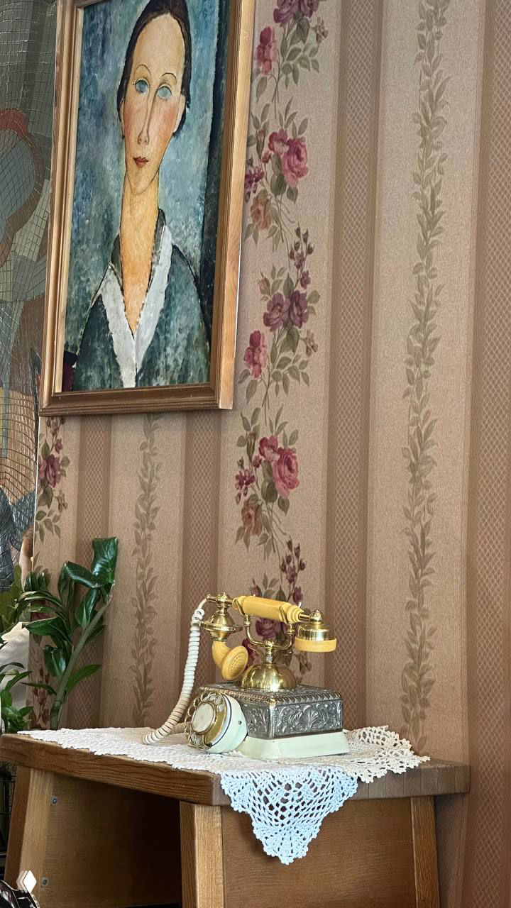 Винтажный золотой телефон на кружевной салфетке, рядом картина и цветочные обои — уютный уголок для ретрита и встреч.