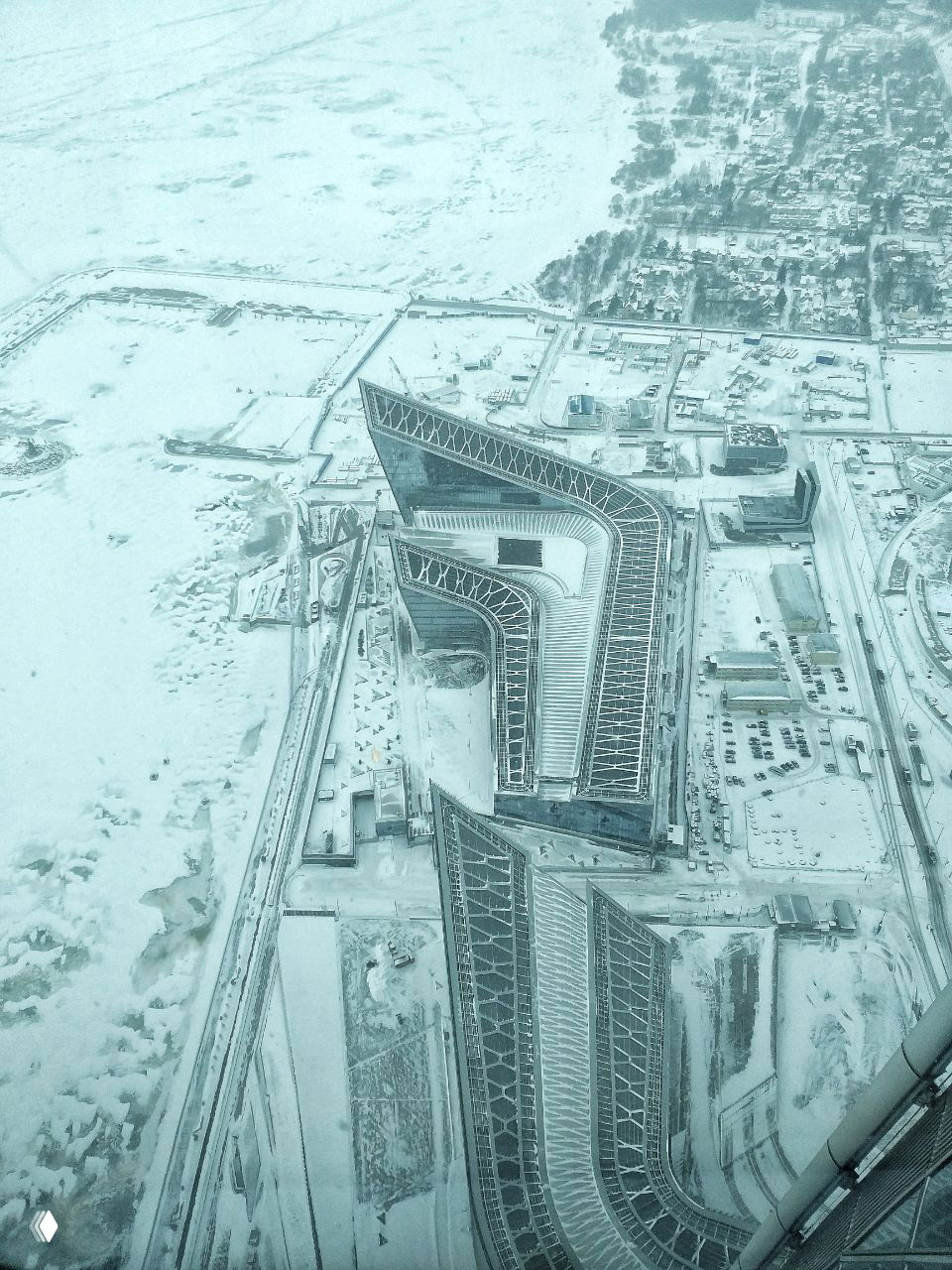 Аэровид сверху на сложный архитектурный силуэт комплекса Лахта‑центра и прилегающие территории, покрытые снегом и льдом вокруг.