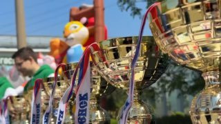 Кубки в крупном плане на фоне участников региональных соревнований «Российский Азимут‑2026», поддержанных ГК «САР».