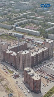 Аэрофотоснимок строительного объекта ГК САР: многоэтажные корпуса находятся в процессе возведения, видны башенный кран, стройтехника и парковка рядом с площадкой.