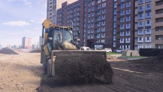 Экскаватор и строительная техника выравнивают временный проезд у многоквартирного дома ЖК «Современник» на стройплощадке, укладка покрытия для уменьшения пыли и грязи.