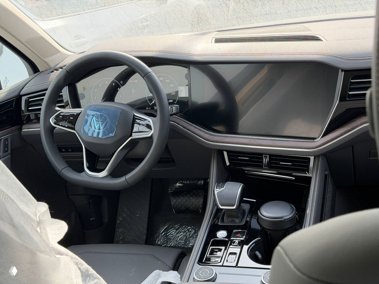 Крупный план рулевого колеса и центрального экрана Volkswagen Touareg, присутствует защитная плёнка на шильдике и экранах приборов.