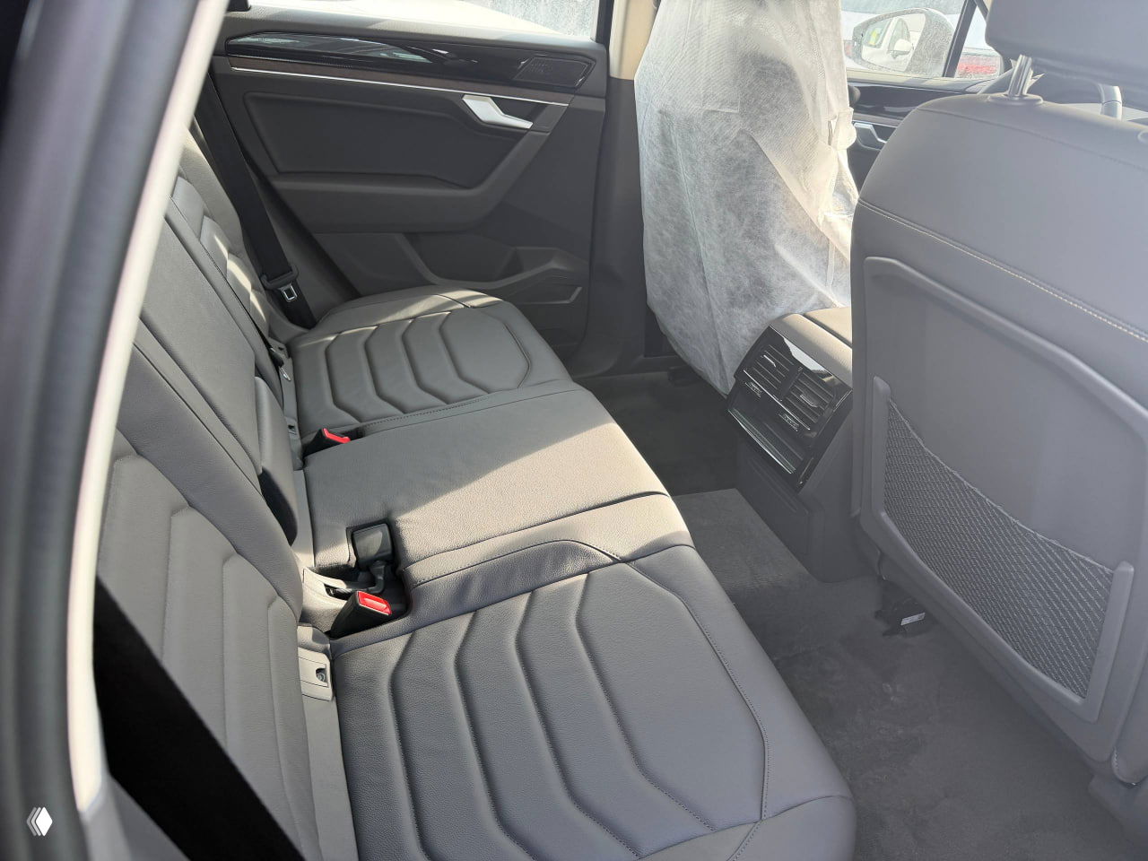 Задний ряд сидений Volkswagen Touareg со стороны двери, виден простор для пассажиров, кожаная обивка и состояние нового автомобиля.