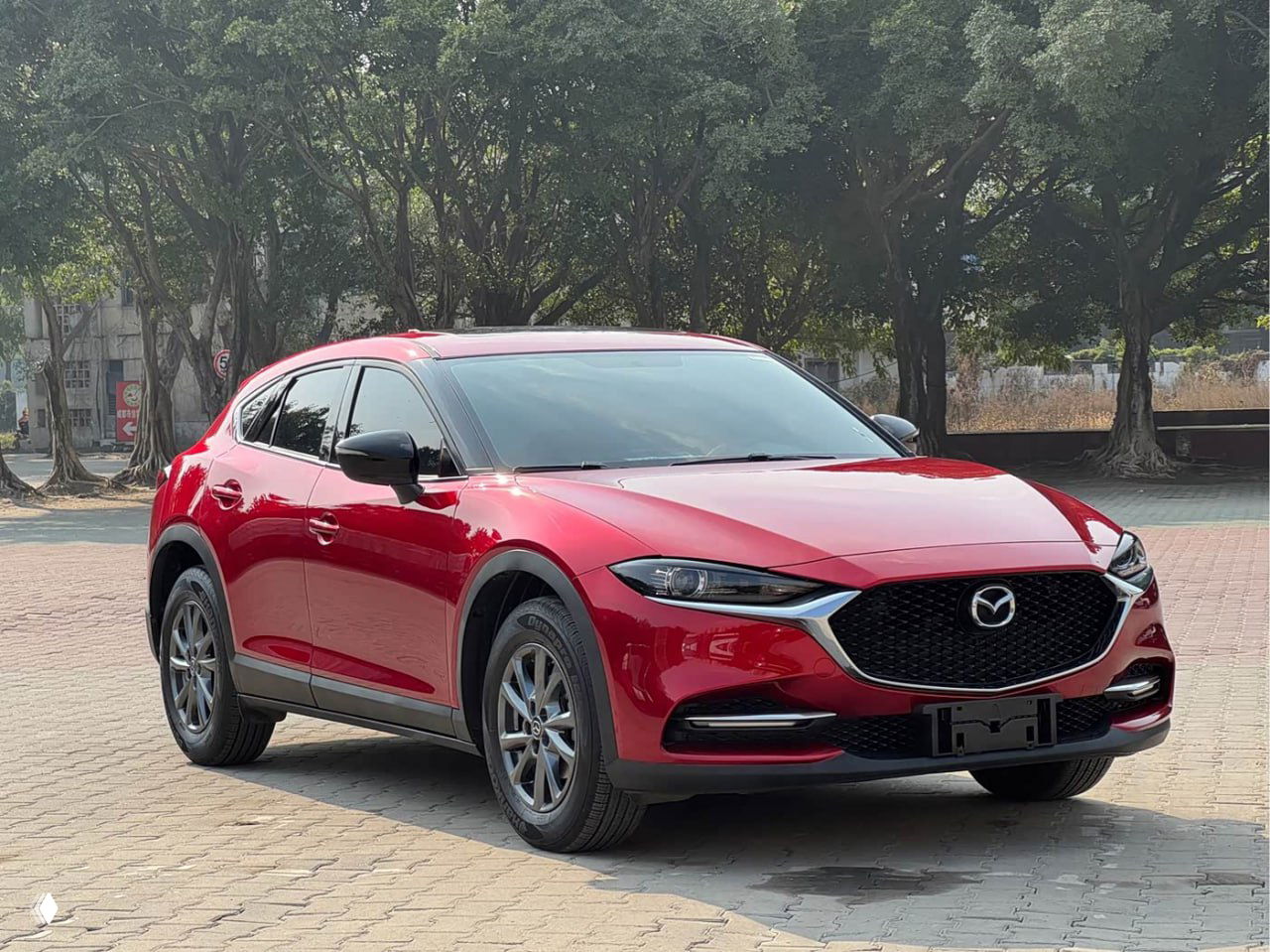 Mazda CX-4 красного цвета, вид три четверти спереди на асфальтовой площадке; аккуратные колёса и лаковая поверхность кузова на солнце.