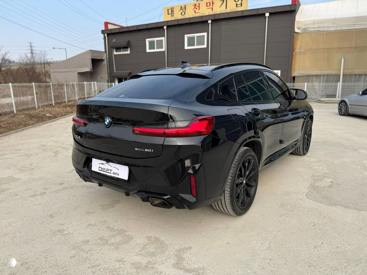 Задне‑левый трёхчетвертной вид BMW X4 — глянцевый чёрный кузов, тонированные задние фонари и спортивный диффузор с патрубками.