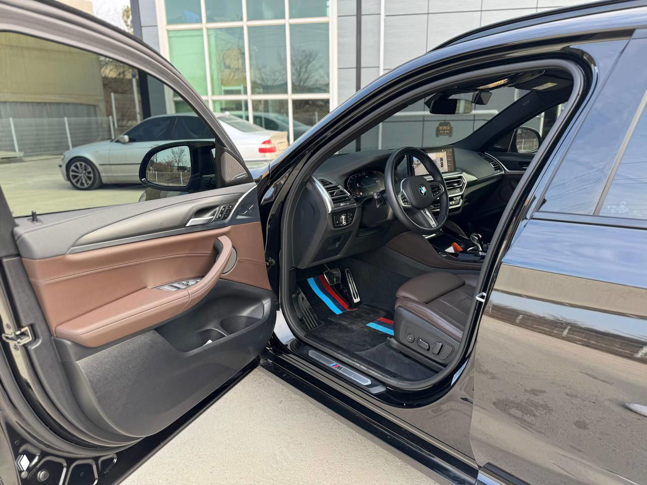 Открытая передняя дверь водителя и вид на салон BMW X4: коричневые кожаные сиденья, алюминиевые подножки и панель с хромированными вставками.